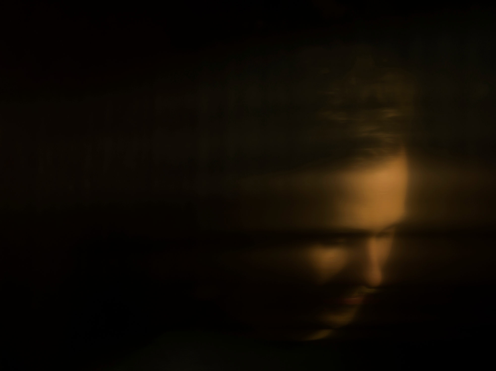 Blurry, dimly-lit image of a person's face partially obscured by darkness, creating a mysterious and abstract effect