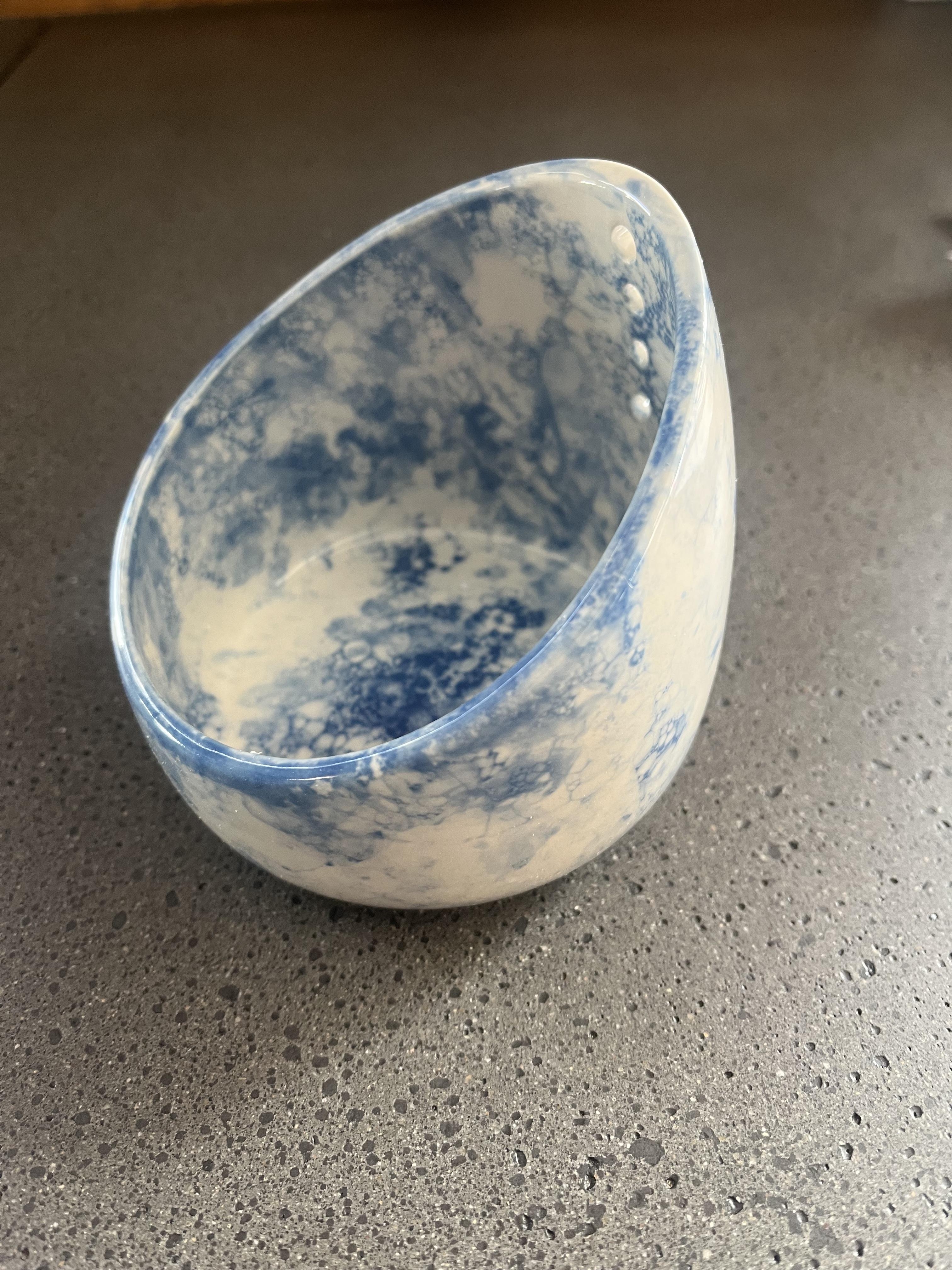 Ceramic bowl with a smooth, rounded shape and a marbled blue and white pattern, placed on a textured surface
