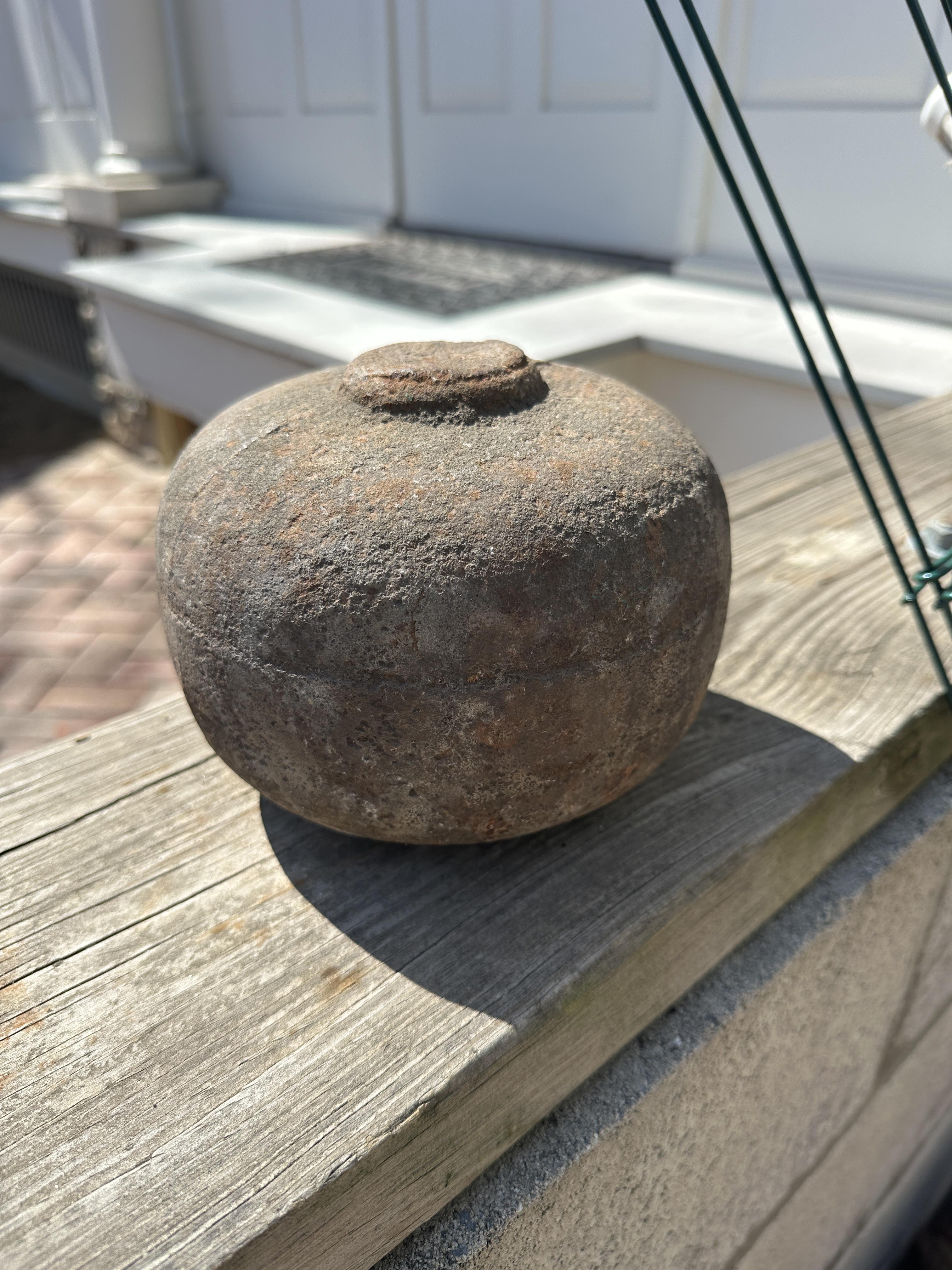 A round, rustic stone object with a flat base and a small raised top, sitting on a wooden railing