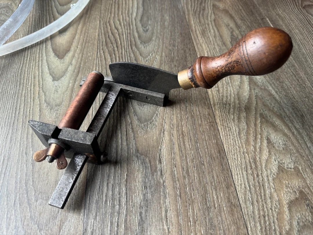 A vintage leather skiving tool with a wooden handle and metal blade on a wooden surface