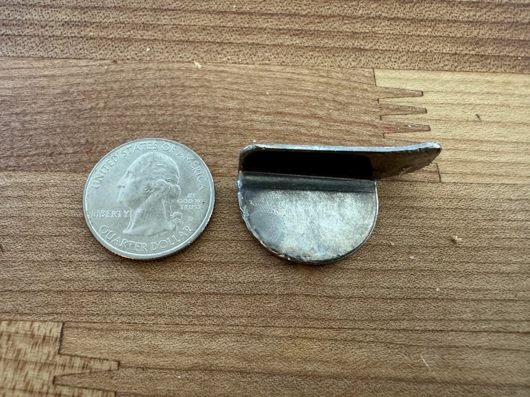 Quarter next to a round metal object with a hinged flap on a wooden surface