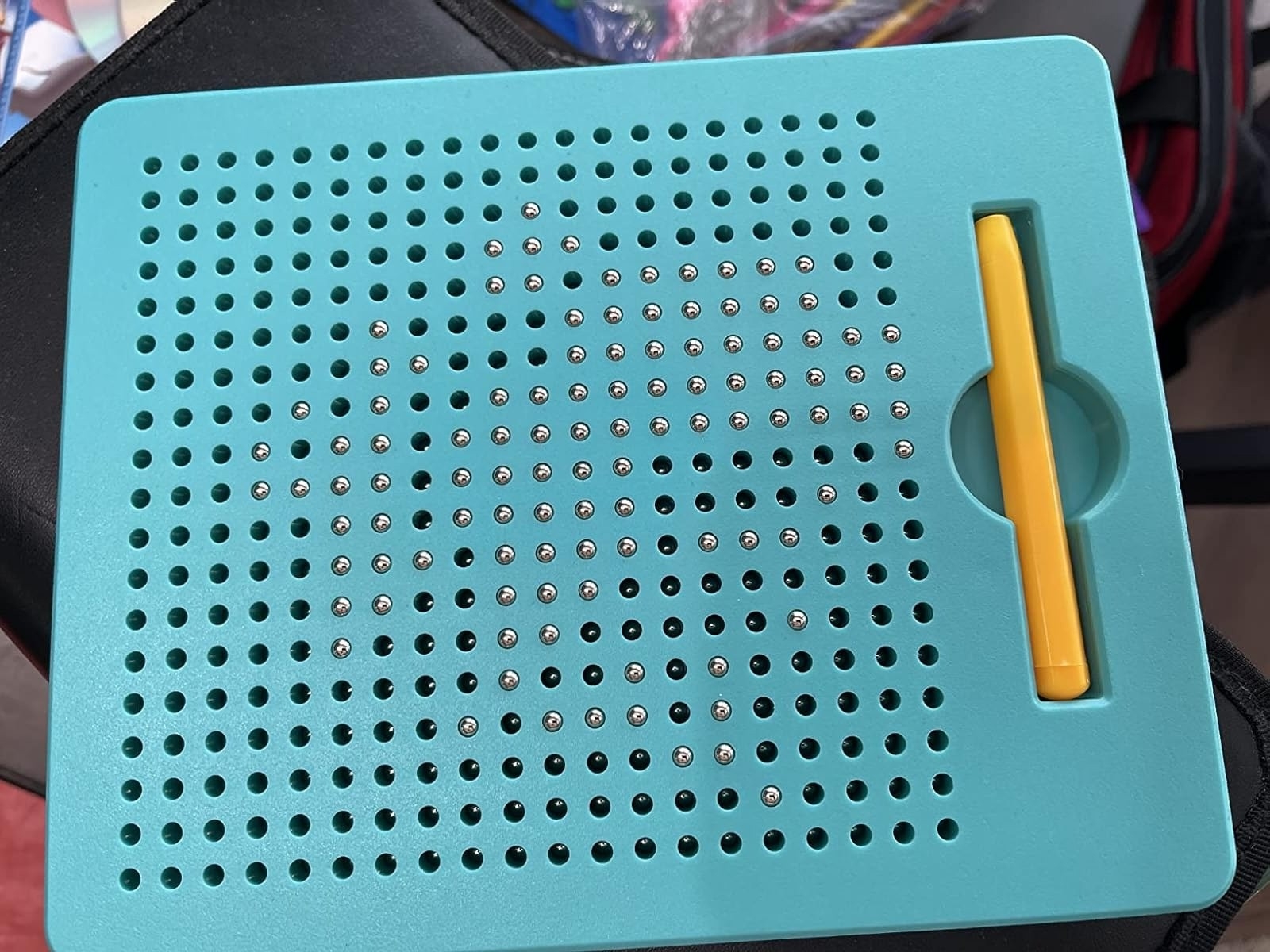 Magnetic drawing board with grid of holes and metal balls inside, featuring a yellow stylus for creating designs by lifting the balls