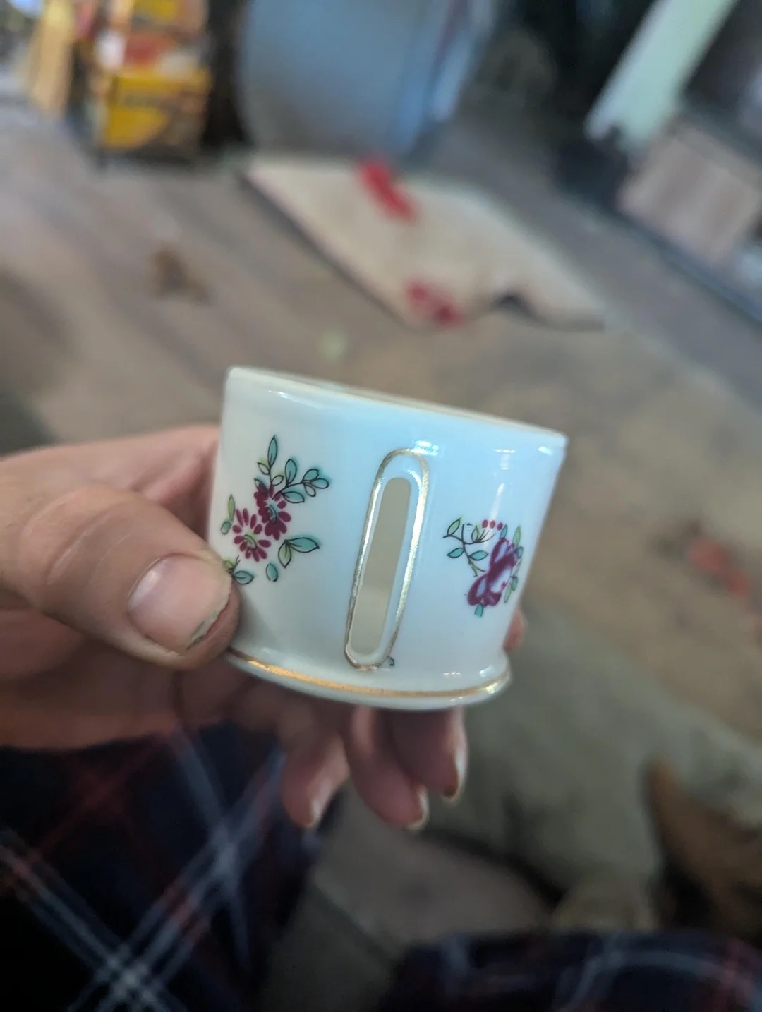 Person holding a small, decorative cup with floral designs, indoors