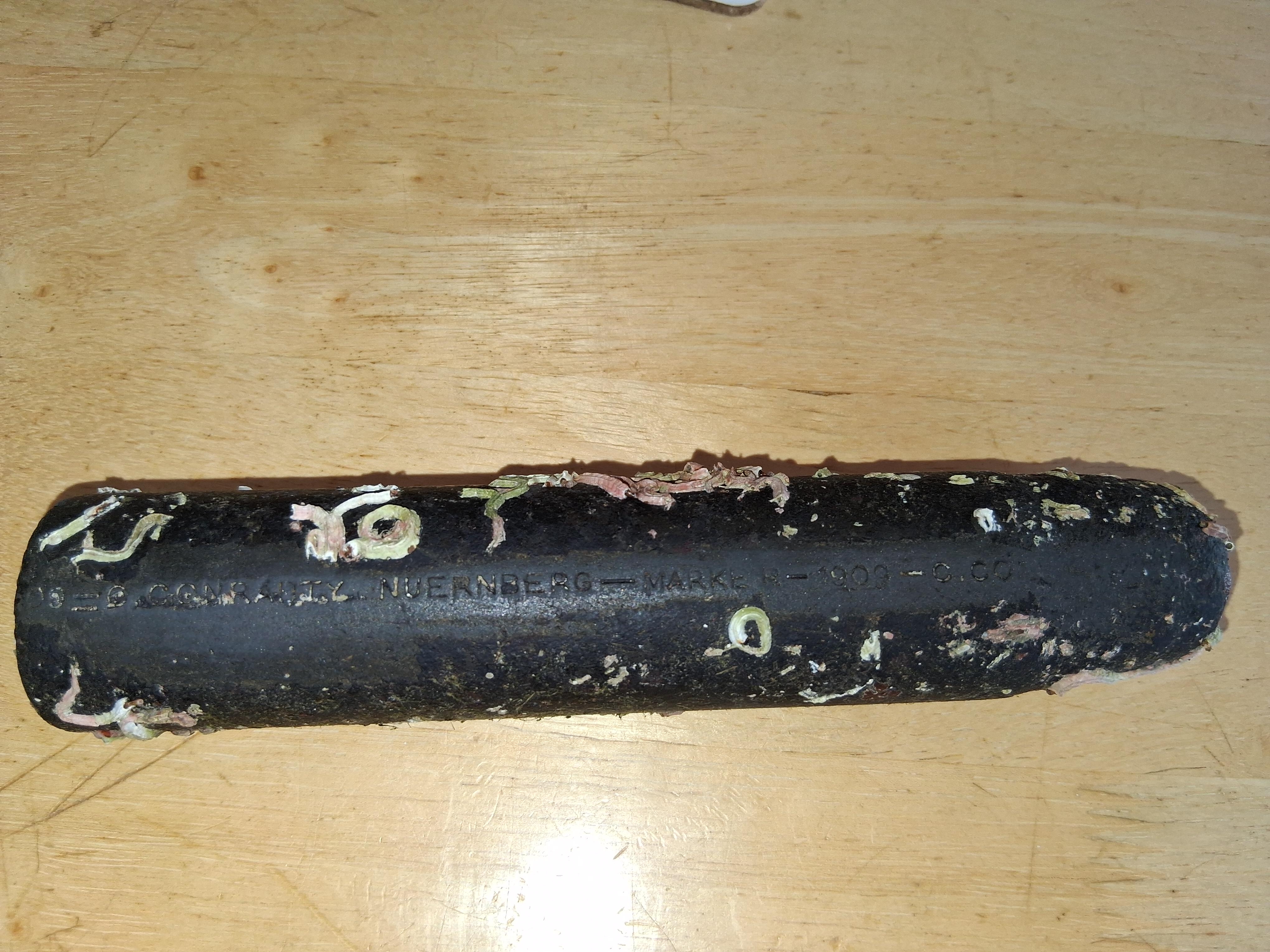 A worn black rubber baton with some numbers and letters embossed on its surface, resting on a wooden table