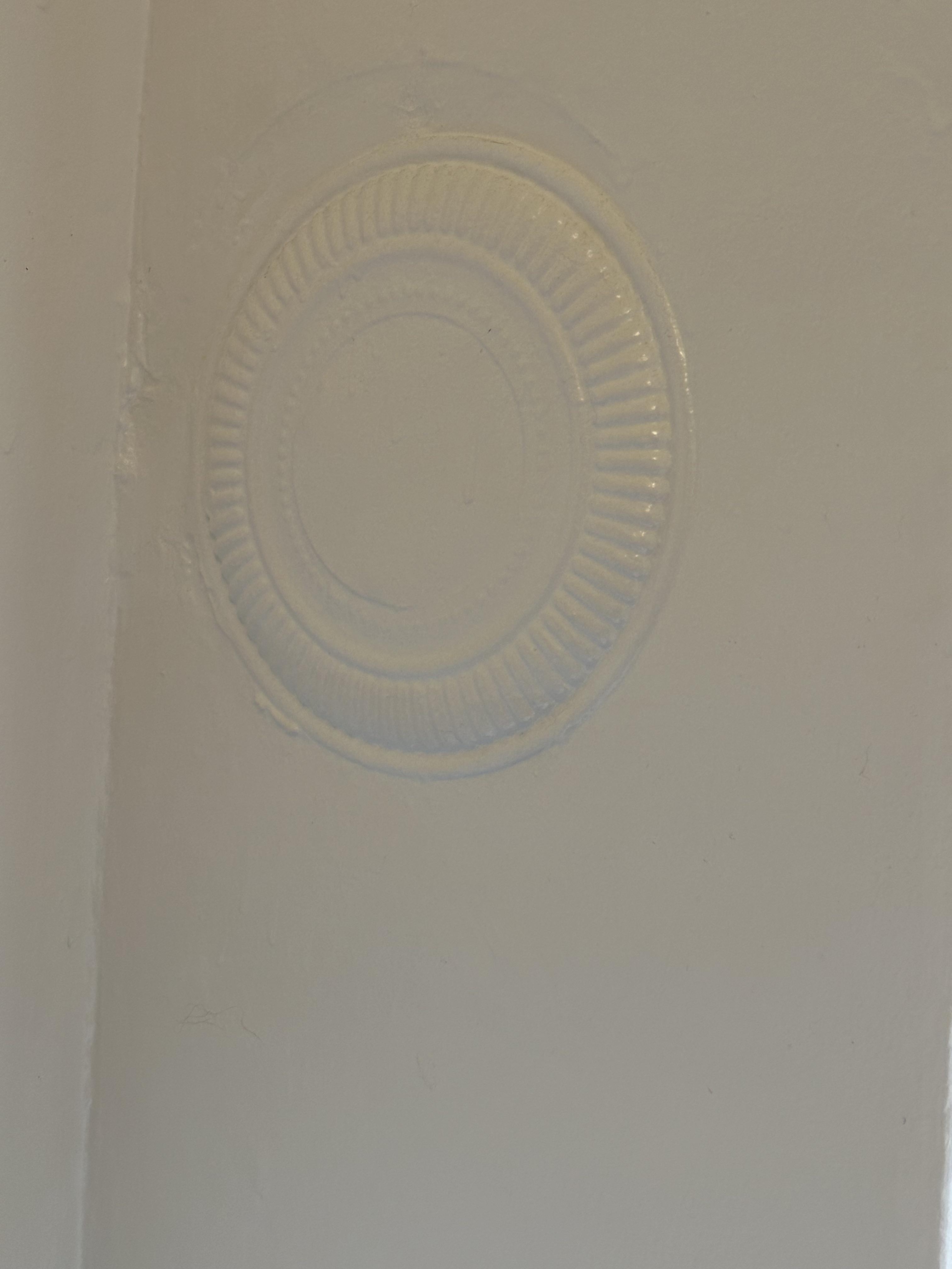 A paper plate is painted over and pressed against the ceiling, creating a makeshift decorative ceiling medallion