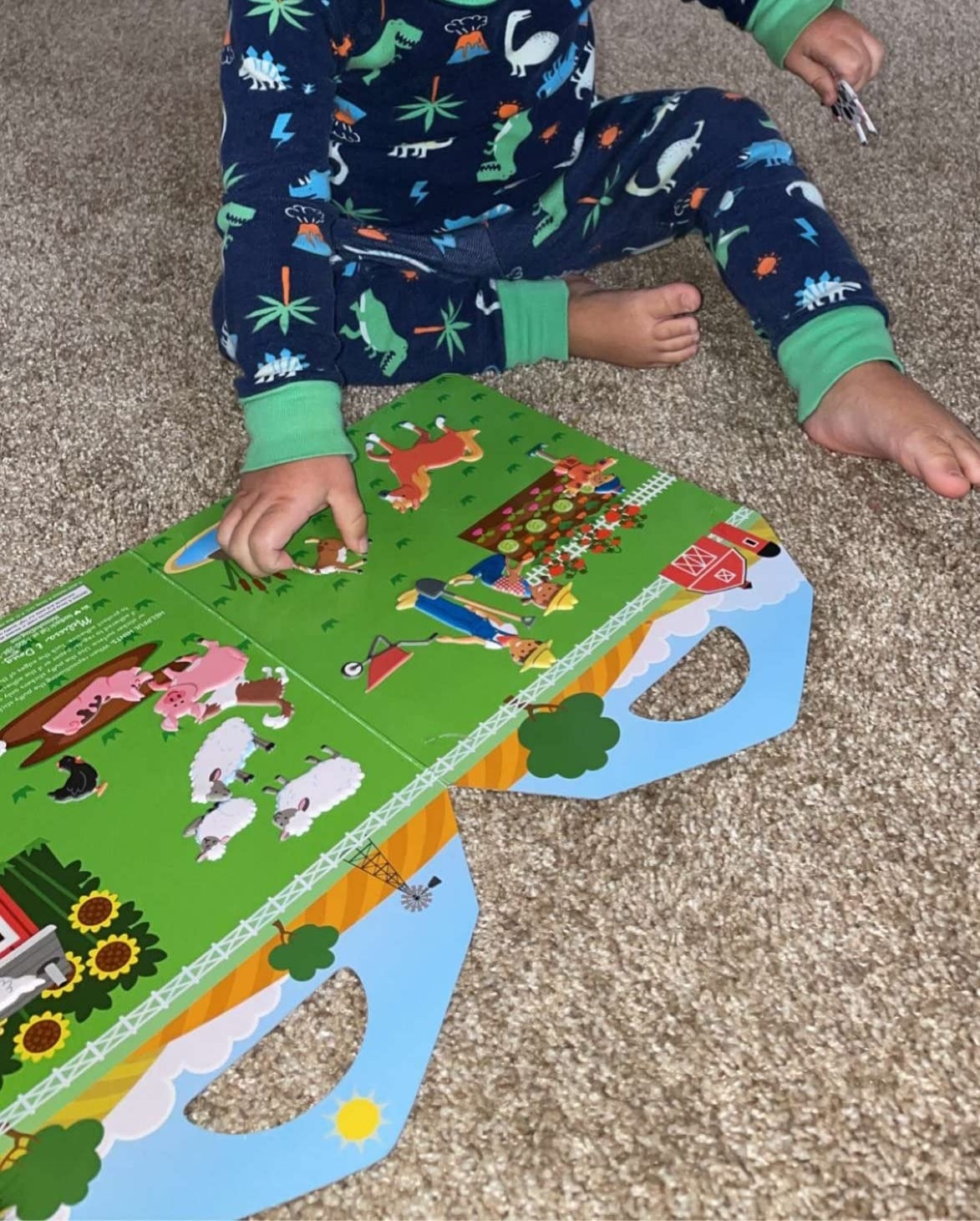 Child in animal-themed pajamas playing with a farm-themed pop-up book on a carpeted floor