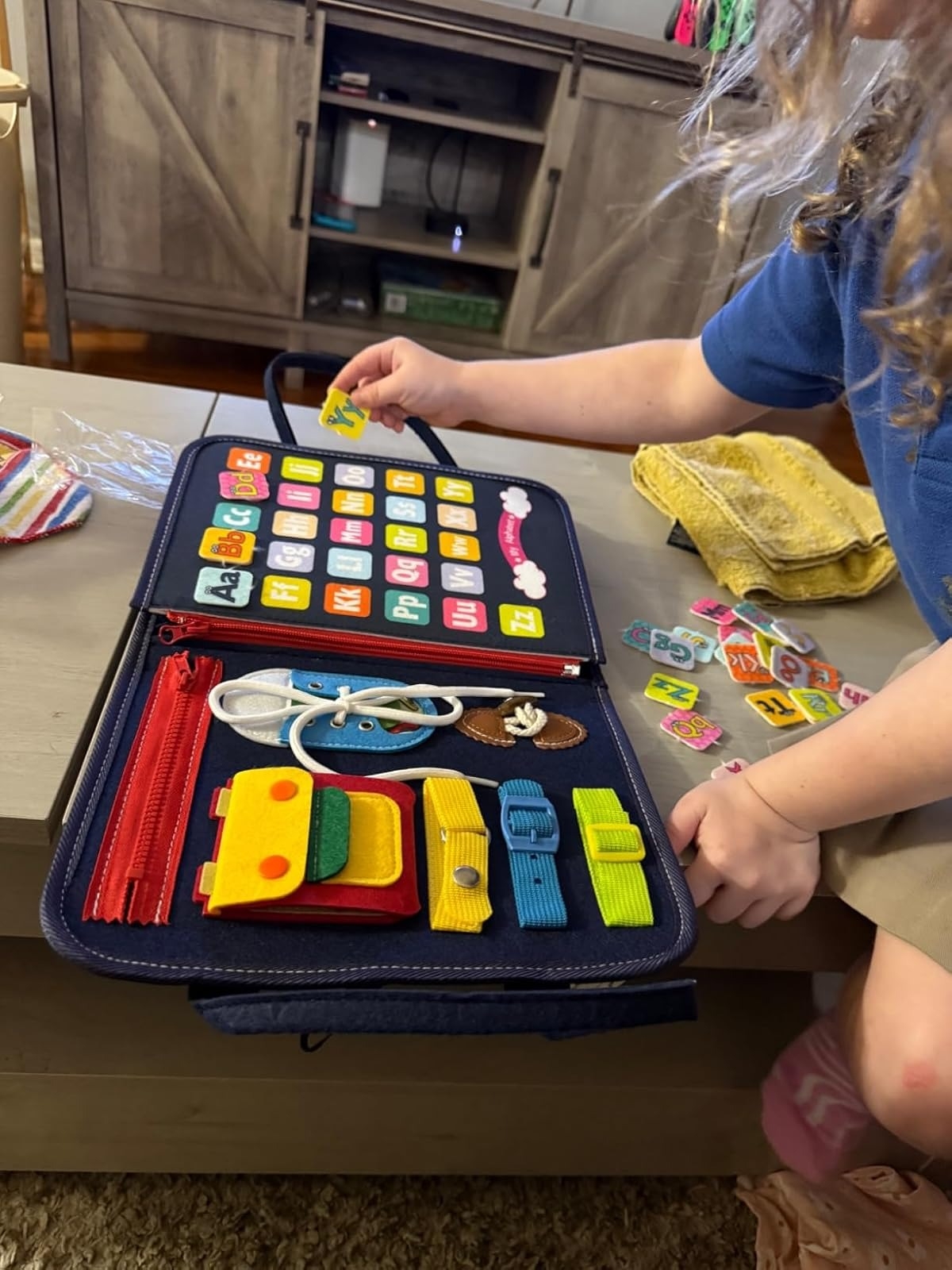 Child playing with an interactive learning binder featuring zippers, buttons, and Velcro for educational play