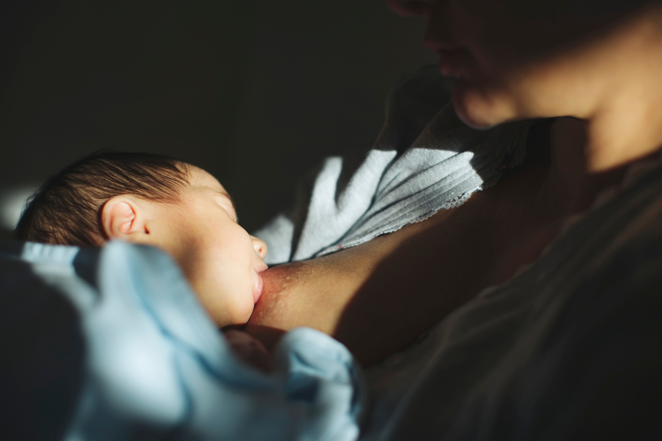 A person is breastfeeding a baby wrapped in a blanket, shown in a tender and intimate moment