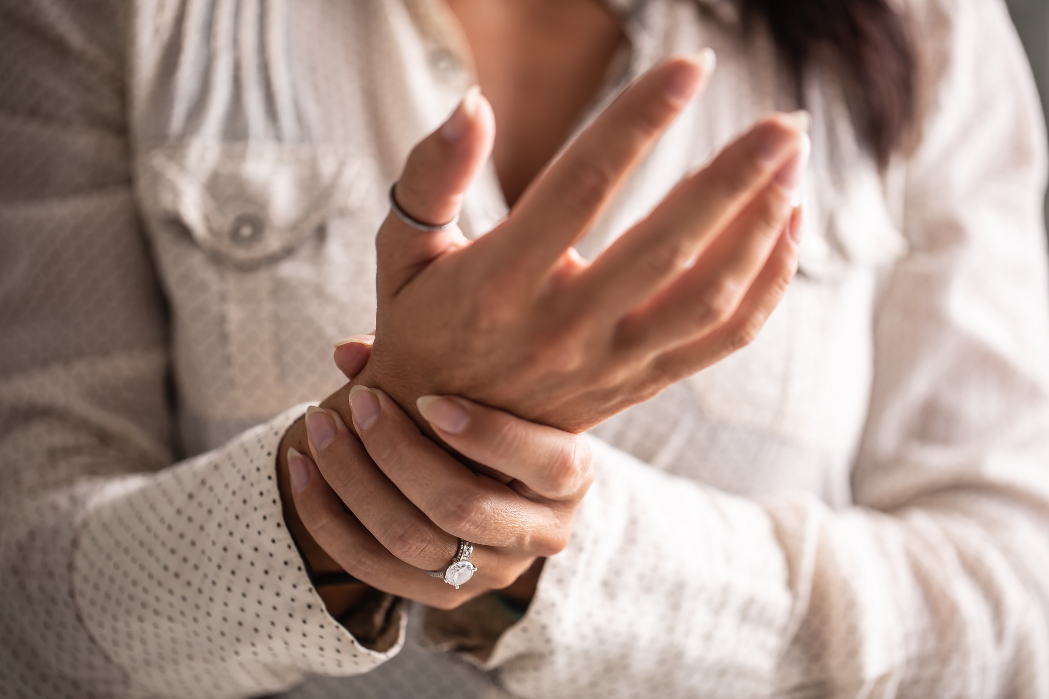 Person wearing a ring gently rubs their wrist, suggesting discomfort or soothing gesture. They are wearing a textured shirt