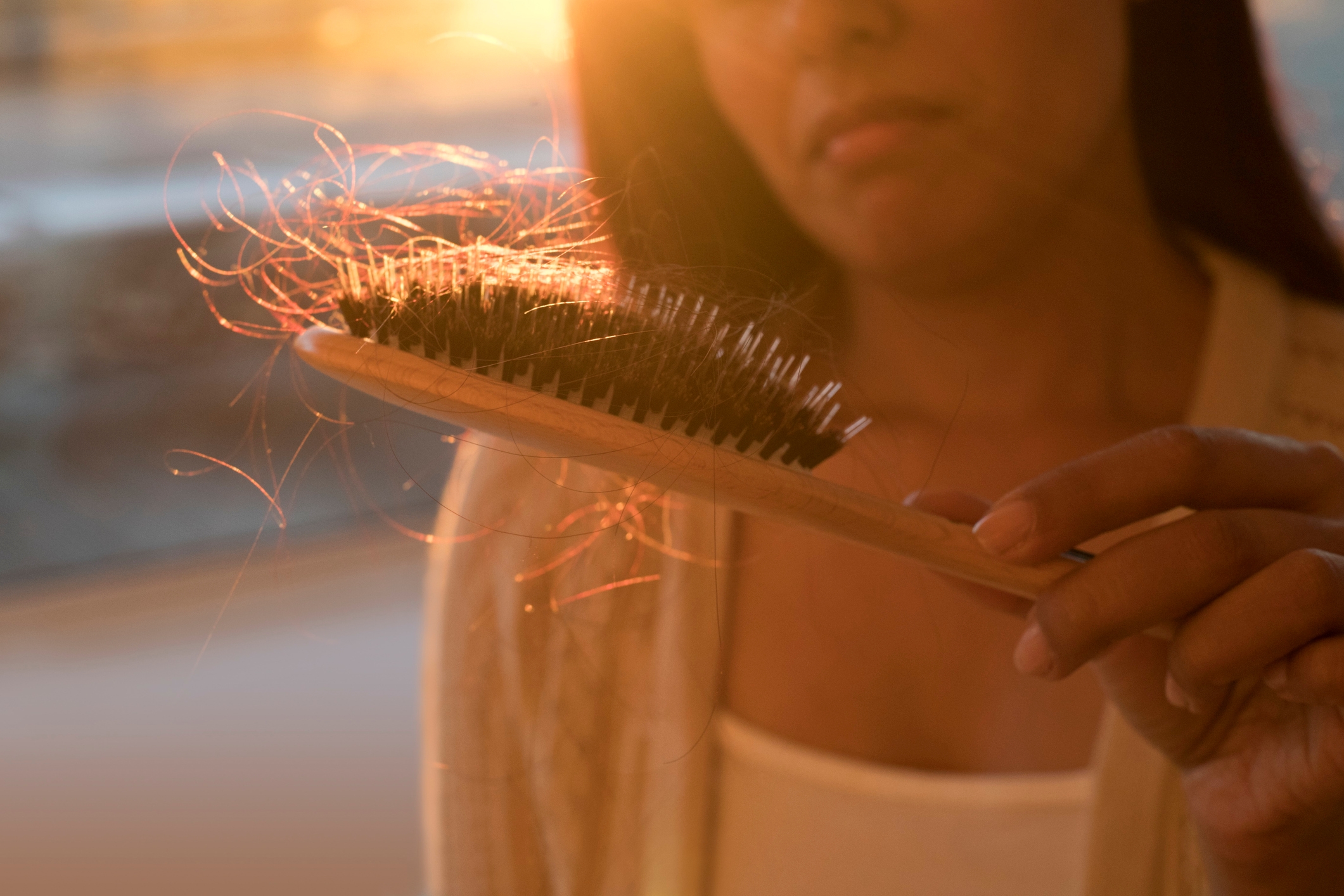 A person holds a hairbrush with visible hair strands, gazing at it thoughtfully