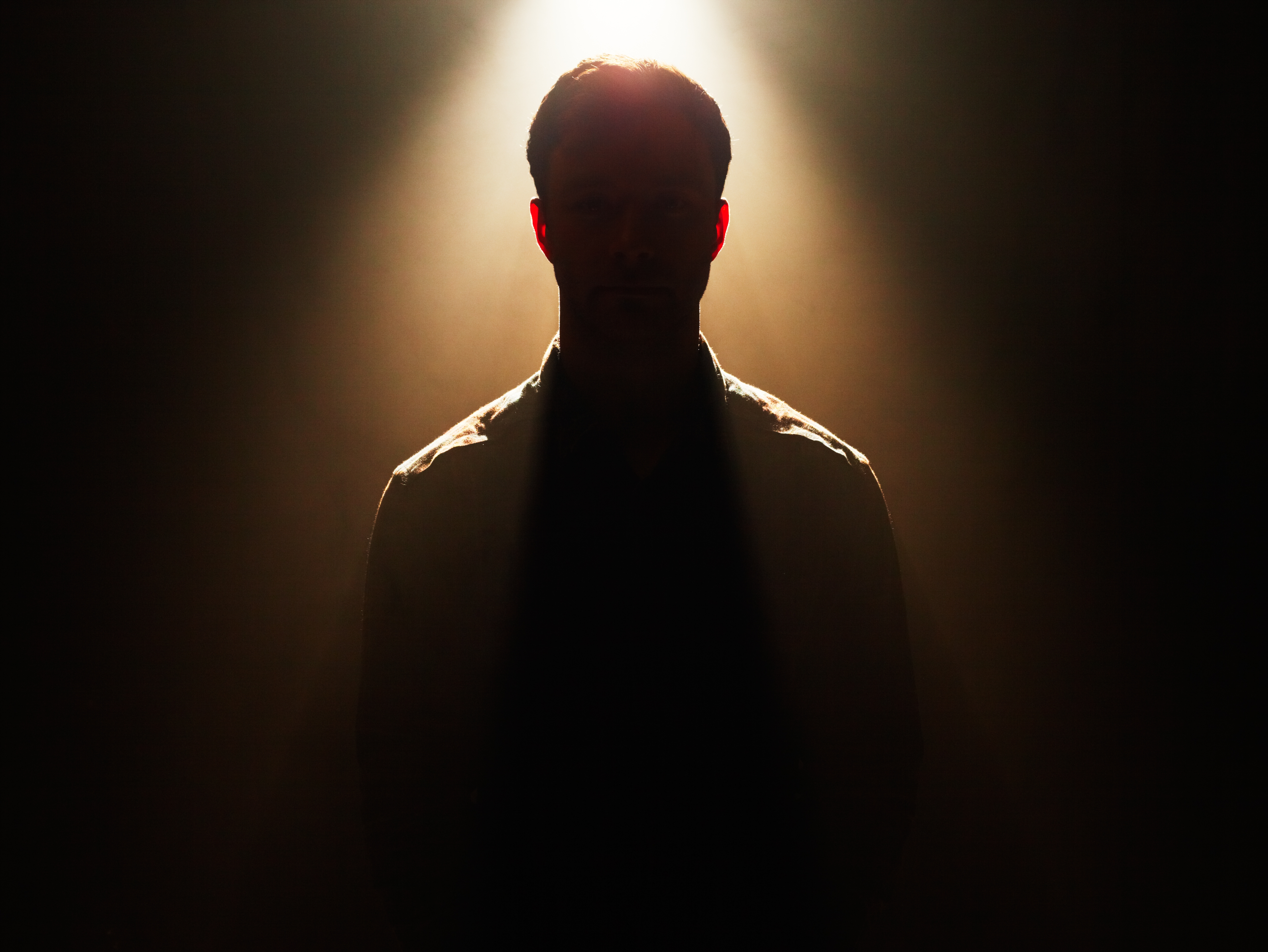 Silhouetted person standing under spotlight, face obscured, creating a dramatic atmosphere