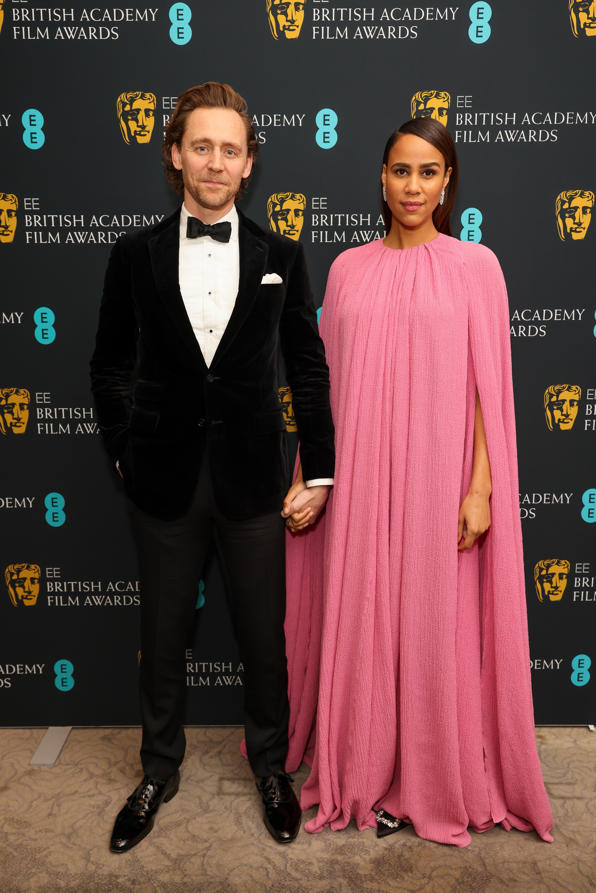 Tom and Zawe holding hands on a red carpet