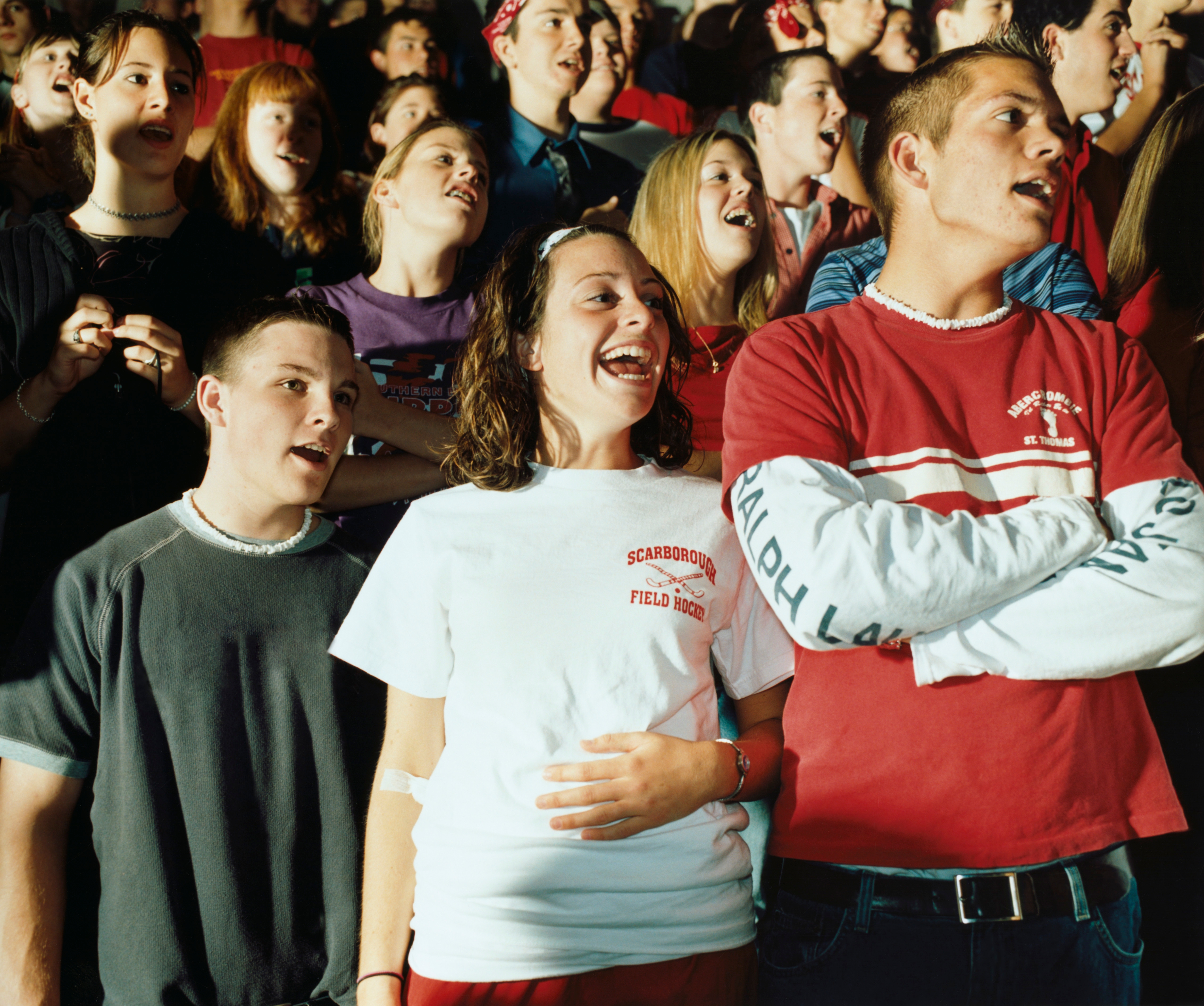 A group of young people at a lively event, wearing casual T-shirts, smiling, and interacting with each other