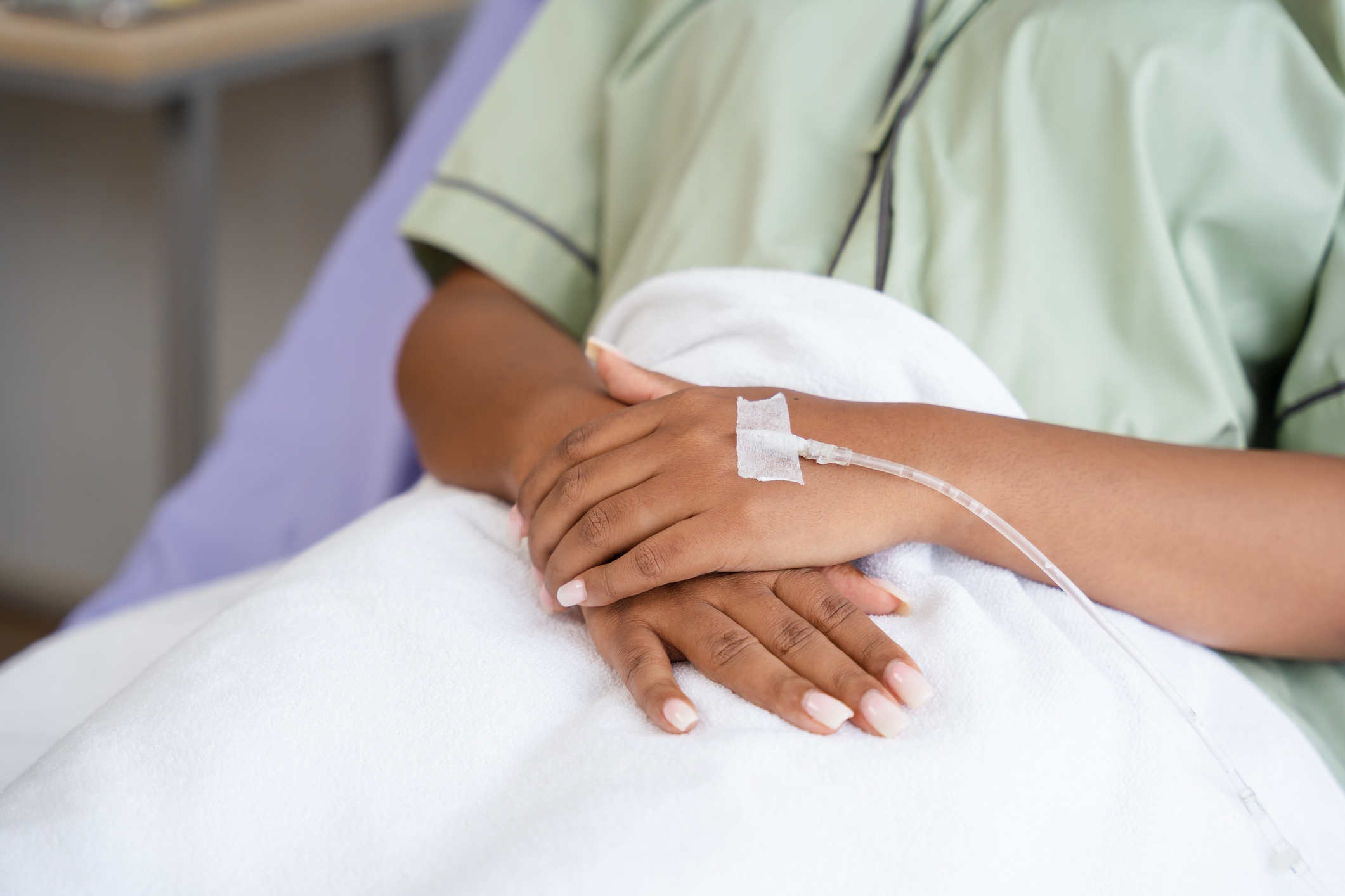 Person resting in a hospital bed, wearing a medical gown with an IV drip attached to their hand