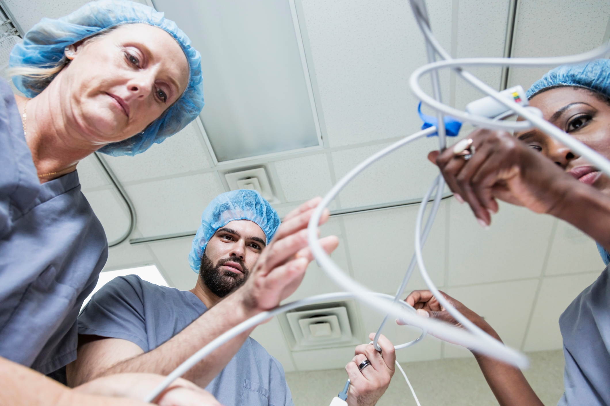 Medical team in scrubs and hair caps focusing on a cluster of medical equipment, possibly preparing for surgery