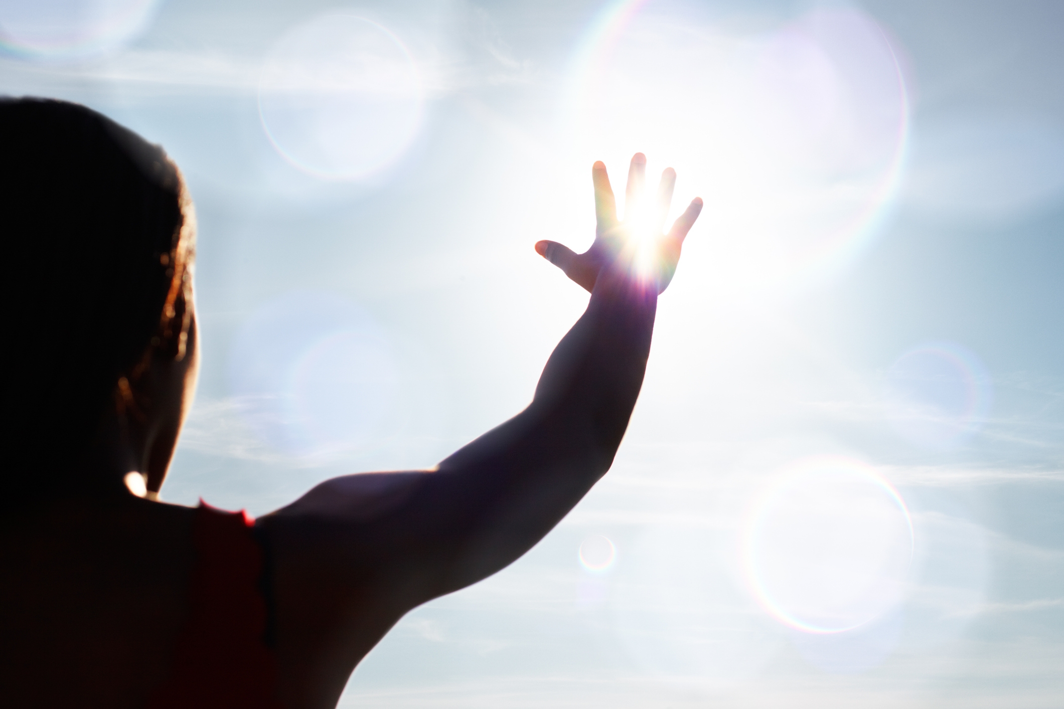 Person reaching towards bright light with an outstretched hand, lens flare effects seen around them