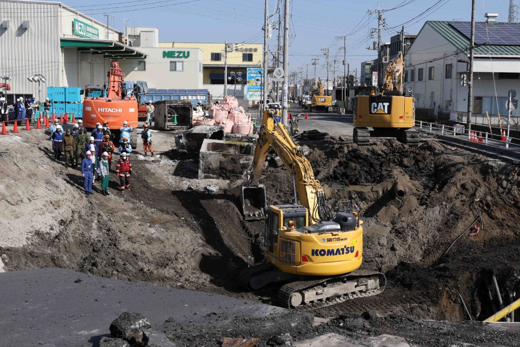 Construction site with heavy machinery and workers repairing a large sinkhole on a city street
