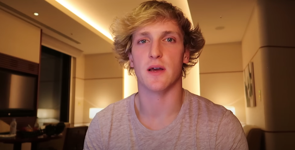 Person with wavy hair in a casual T-shirt sits in a warmly lit room, speaking to the camera