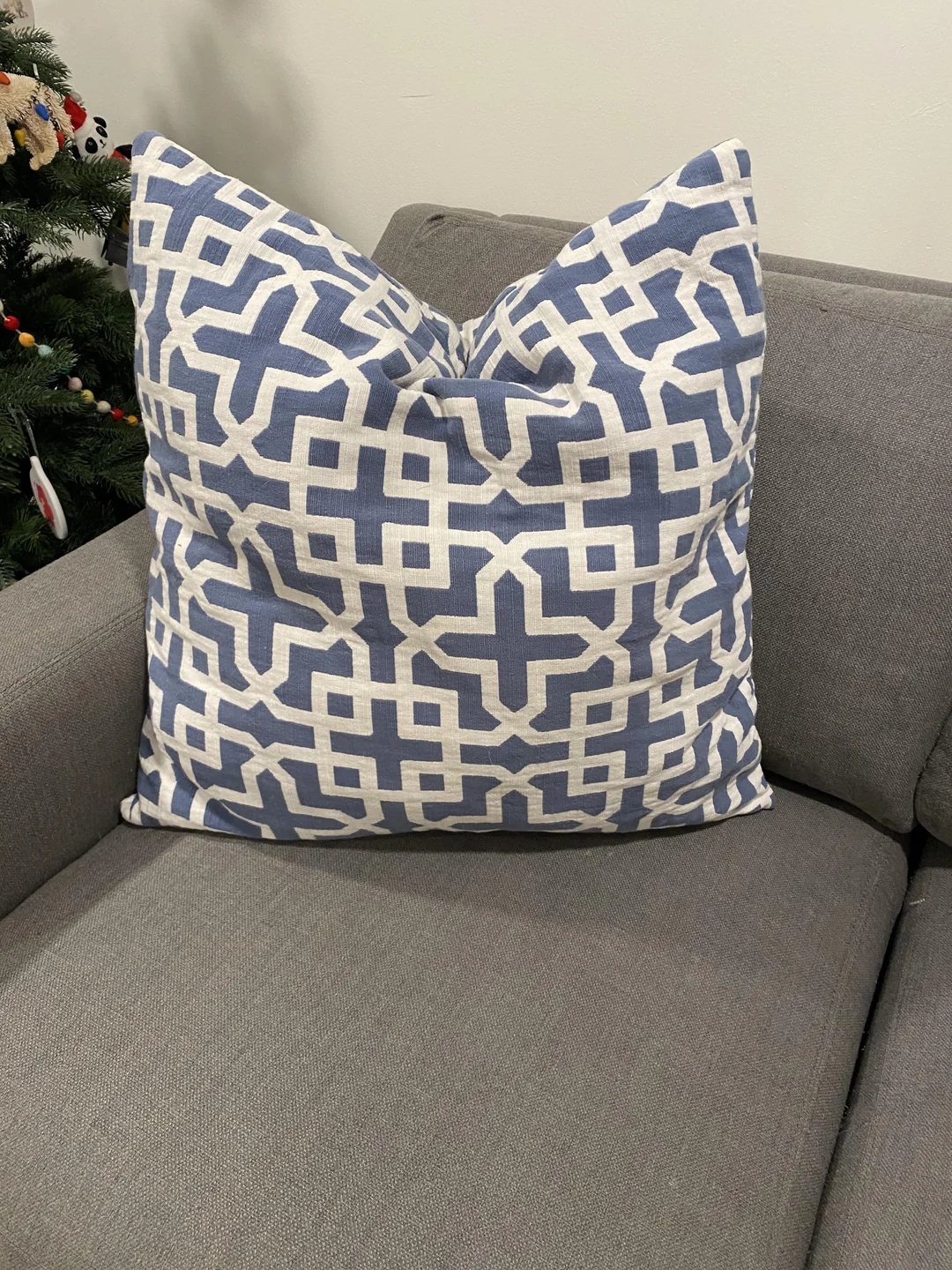 Geometric-patterned pillow on a gray sofa with a glimpse of holiday decorations in the background