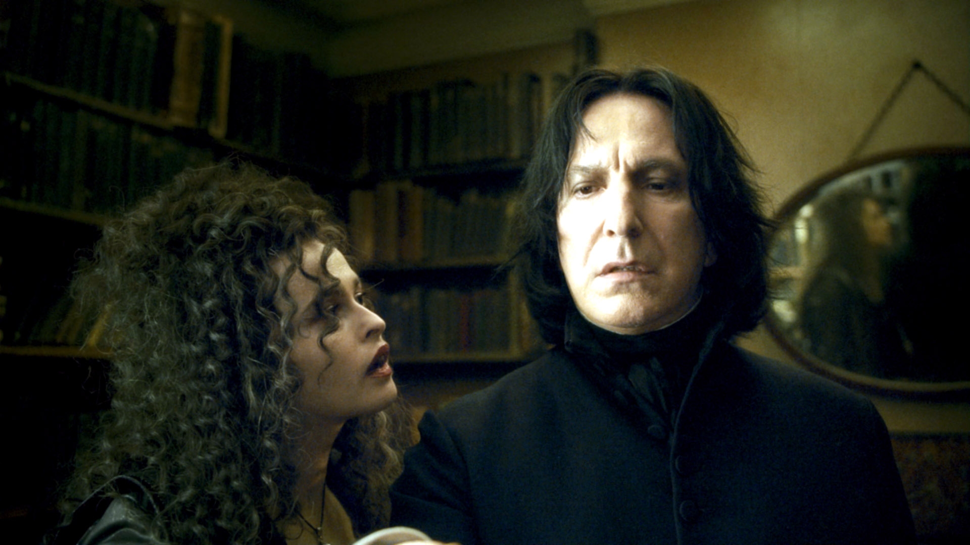 Two characters in a dimly lit room, one with long curly hair looking intently at the other, who has straight hair and a long coat. Books line the walls