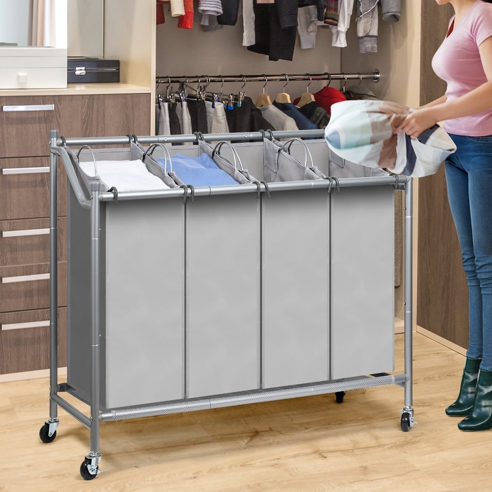 Person placing laundry in a four-compartment rolling hamper in a closet, surrounded by hanging clothes and wooden cabinets