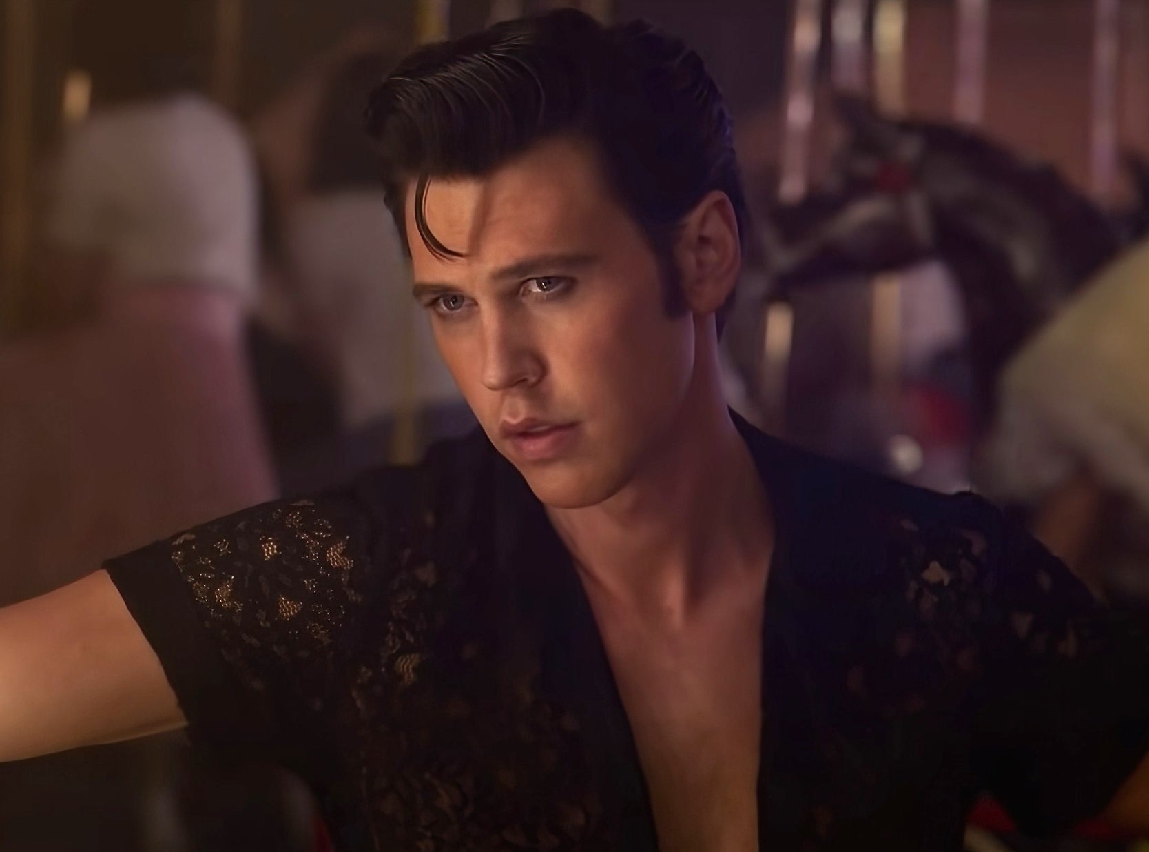 Person in lace shirt leans against a wall, gazing into the distance, appearing thoughtful, in a scene suggestive of a movie or TV show setting