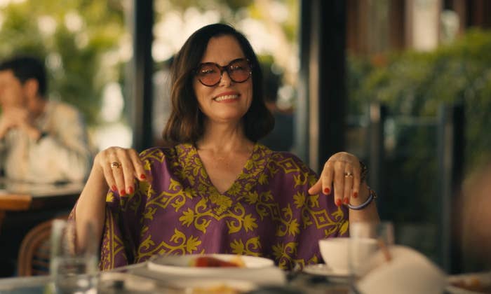 Person smiling at restaurant table, wearing sunglasses and a patterned tunic, with a relaxed and cheerful demeanor