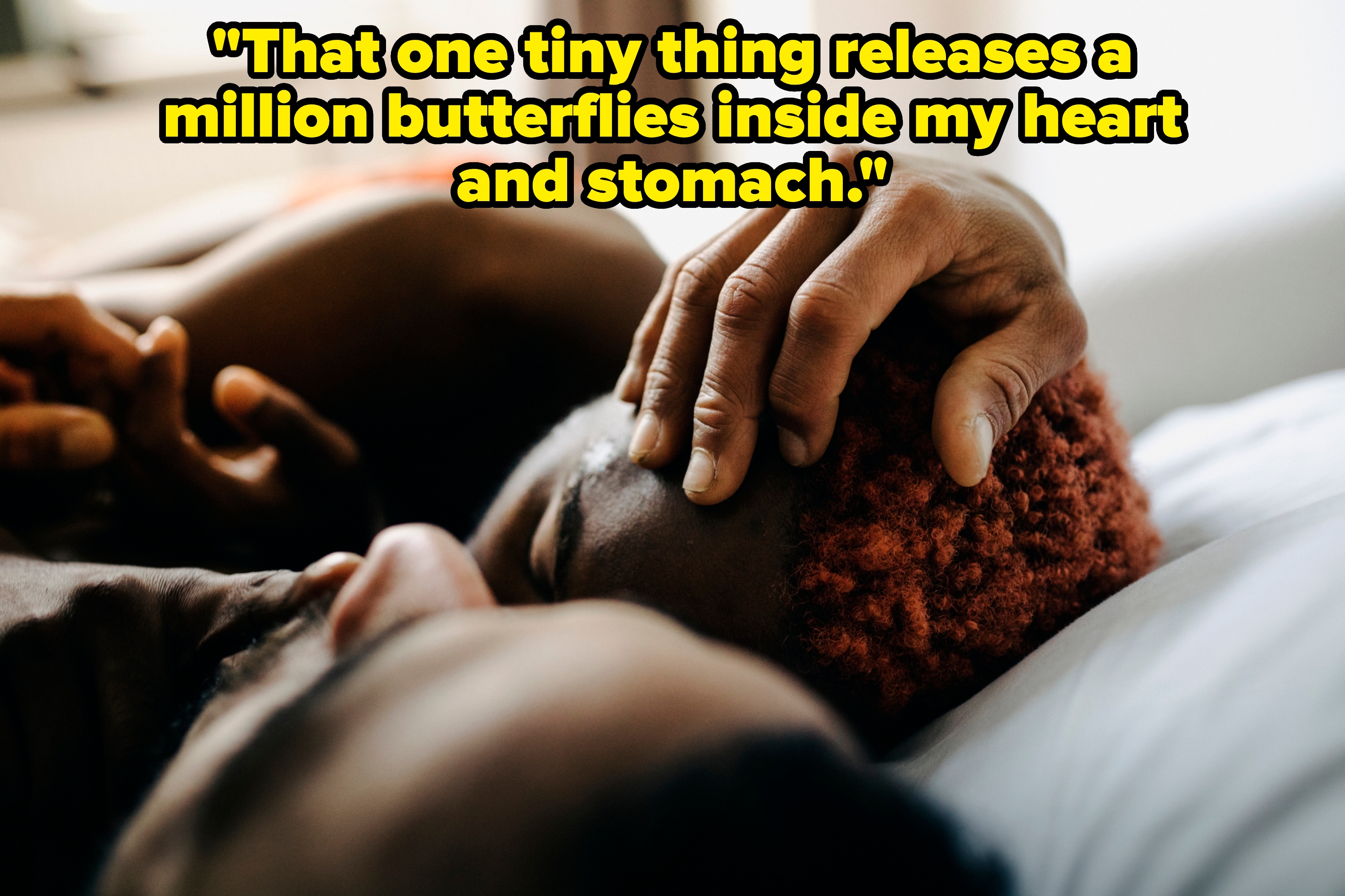 Two people lying close together in bed, showing an intimate and tender moment with one hand gently placed on the other's head