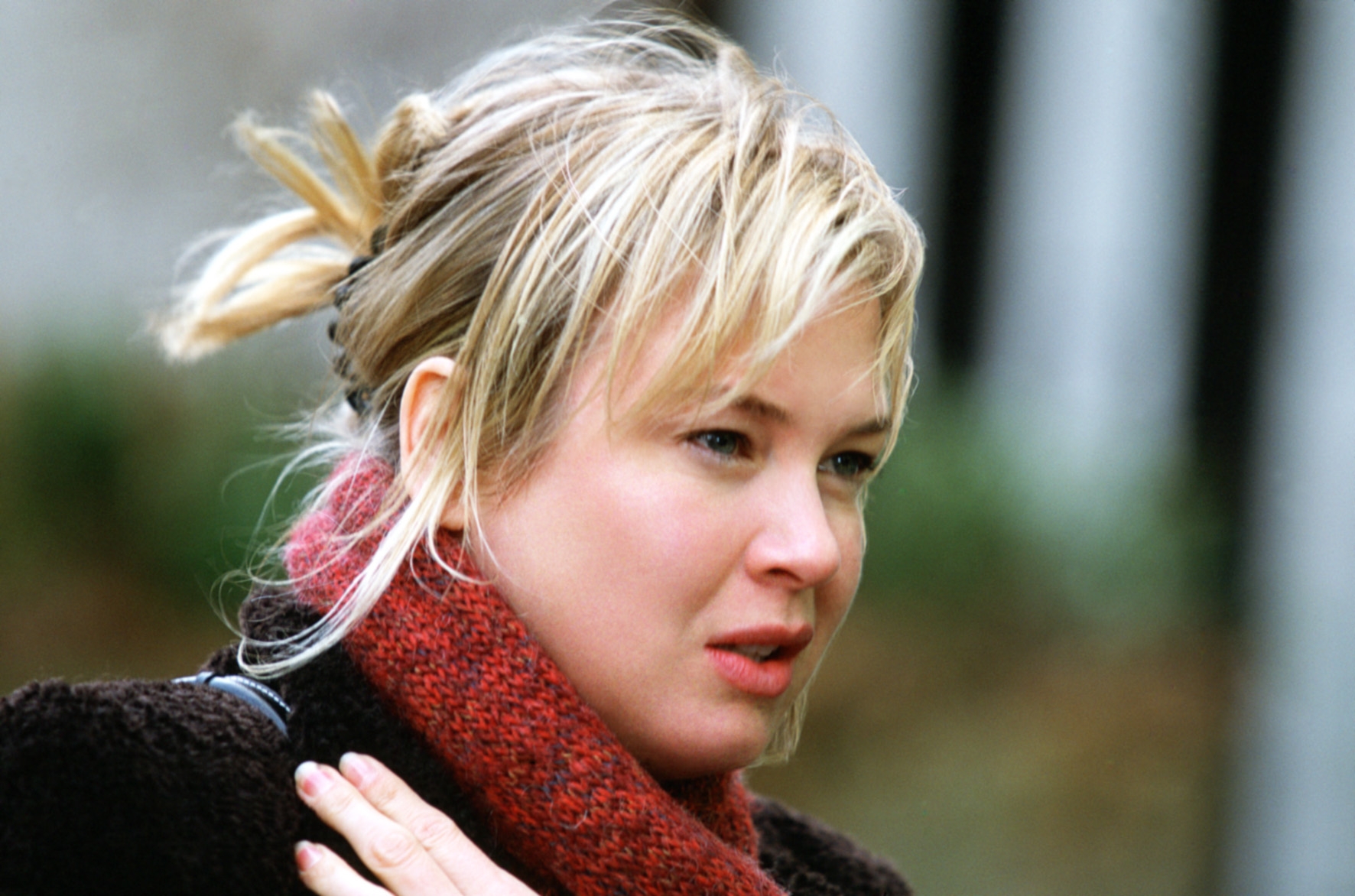 Person outdoors, wearing a warm scarf and coat, looking pensive. Hair is tied back casually