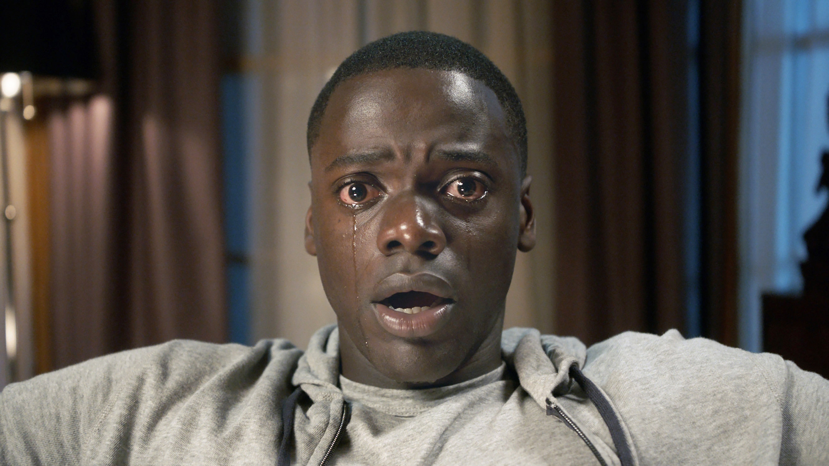 A person with a surprised and emotional expression, tears on their face, sitting in an indoor setting, from a scene in a movie