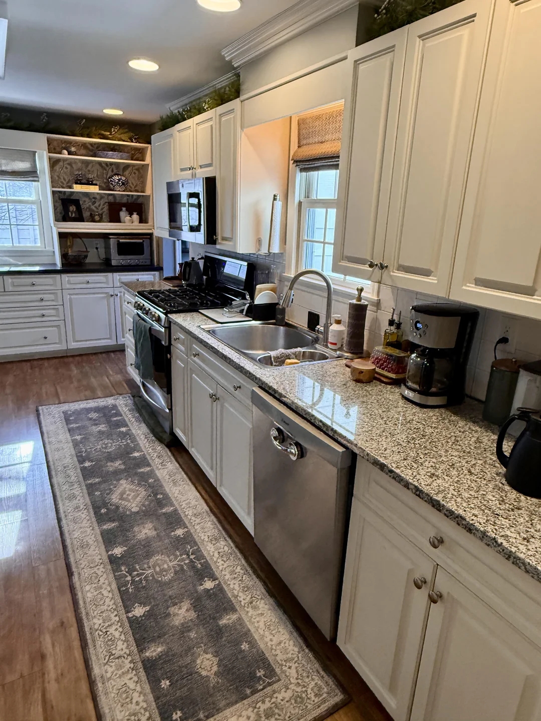 Spacious kitchen with granite countertops, white cabinets, and modern appliances. A patterned runner rug covers the wooden floor