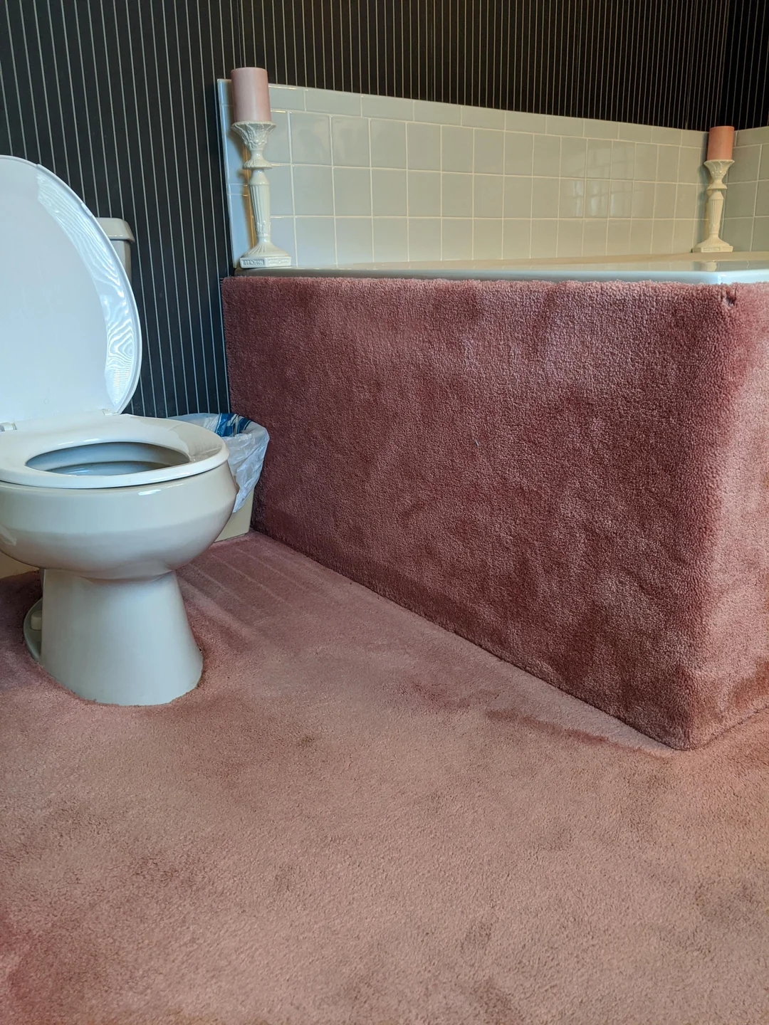 Bathroom with carpeted floor and bathtub exterior, showing a toilet and candleholders on the tub ledge