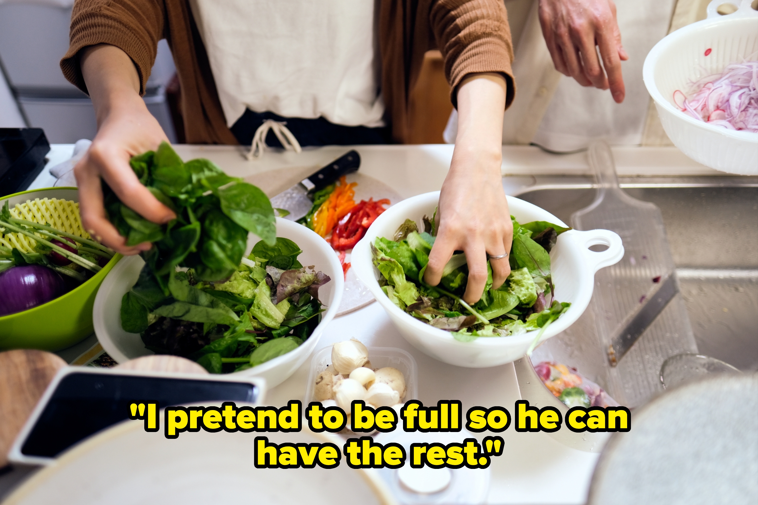 Hands preparing fresh salad with greens, mushrooms, and sliced vegetables in a kitchen setting