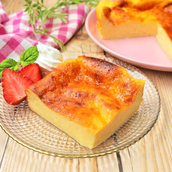 ガラスの皿にケーキ、イチゴ、クリームが添えられた一切れ。背景にチェック柄の布。