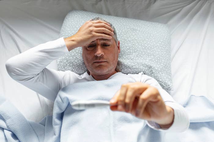 Man in bed looking stressed while holding a thermometer, checking his temperature