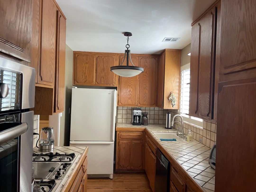 A small kitchen featuring wooden cabinets, a white refrigerator, a tile backsplash, and stainless steel appliances