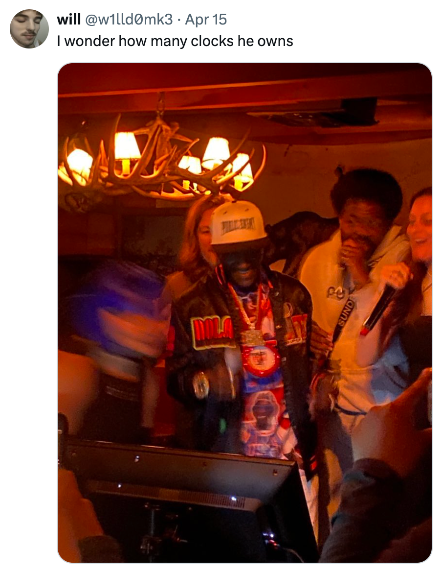 Group of people singing karaoke, one wearing a baseball cap and a jacket with "DOAK" in bold letters, under rustic lighting