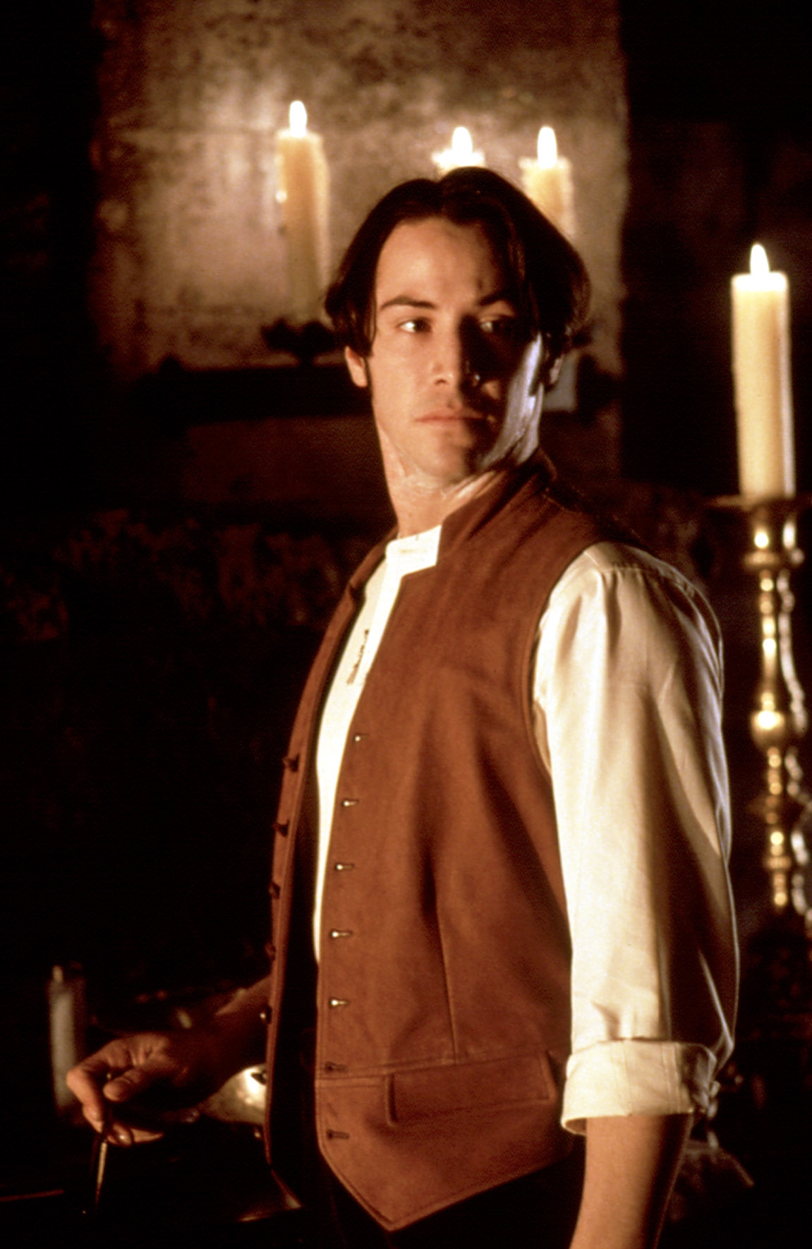 Person in historical costume with a vest, standing by candelabras, looking pensive