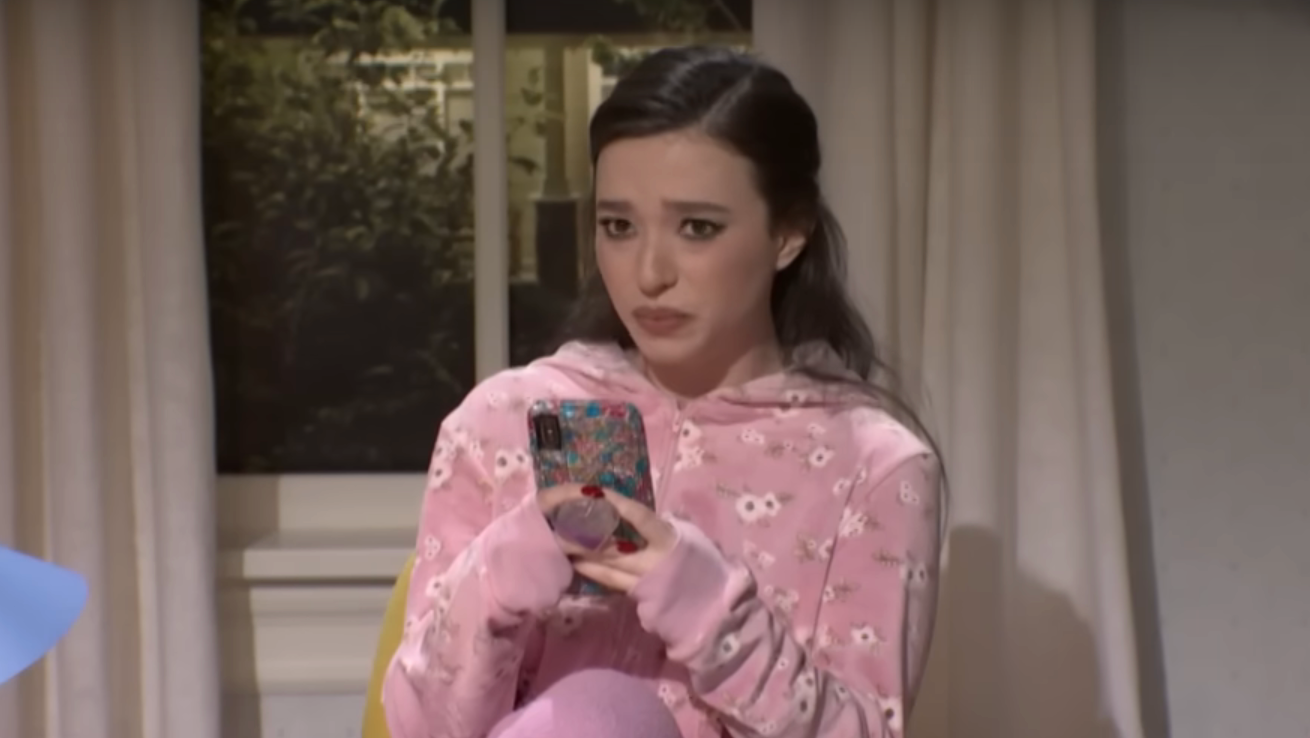 Person in a pink patterned hoodie looks concerned while holding a phone indoors