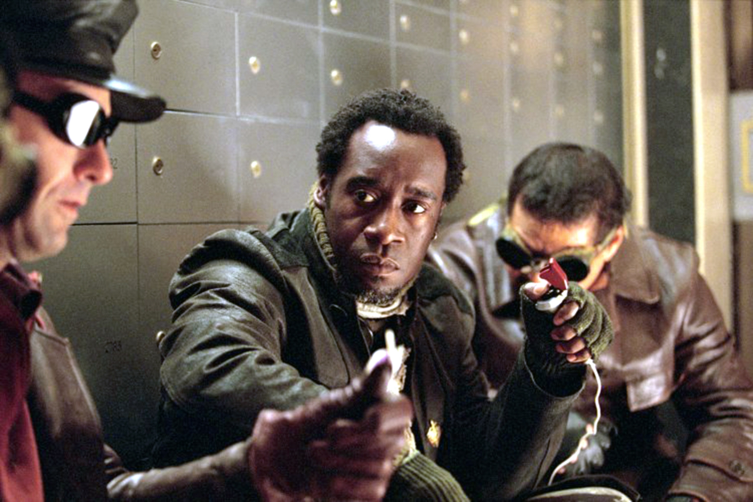 Three people in leather jackets sit tensely against a wall, holding devices, in a scene suggesting a heist or suspenseful mission
