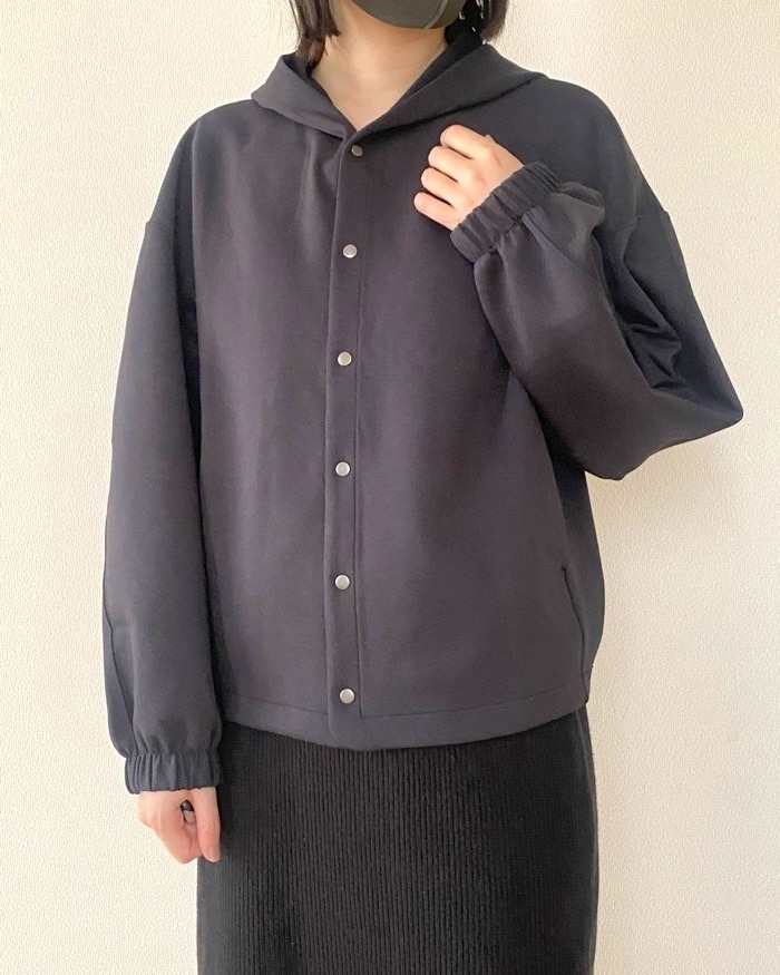 女性がシンプルなフード付きジャケットを着て立っている。ジャケットはカジュアルなスタイル。