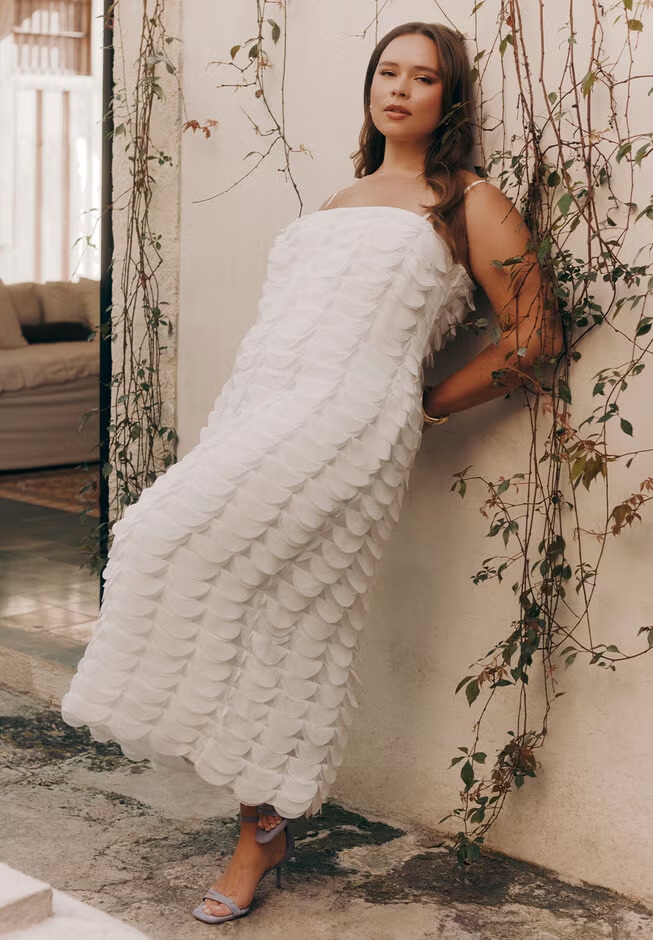 Person in a textured strapless dress leaning against a vine-covered wall in a casual, elegant setting