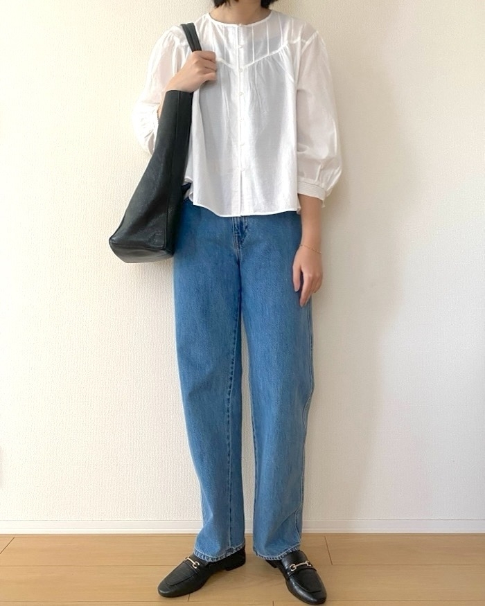 女性が白いブラウスとジーンズを着用し、黒いバッグを肩にかけている様子。カジュアルな装い。