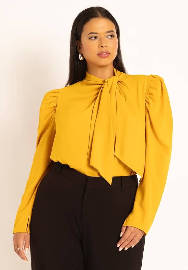 Woman wearing a stylish blouse with a large bow detail and long puffed sleeves, ideal for chic, professional outfits