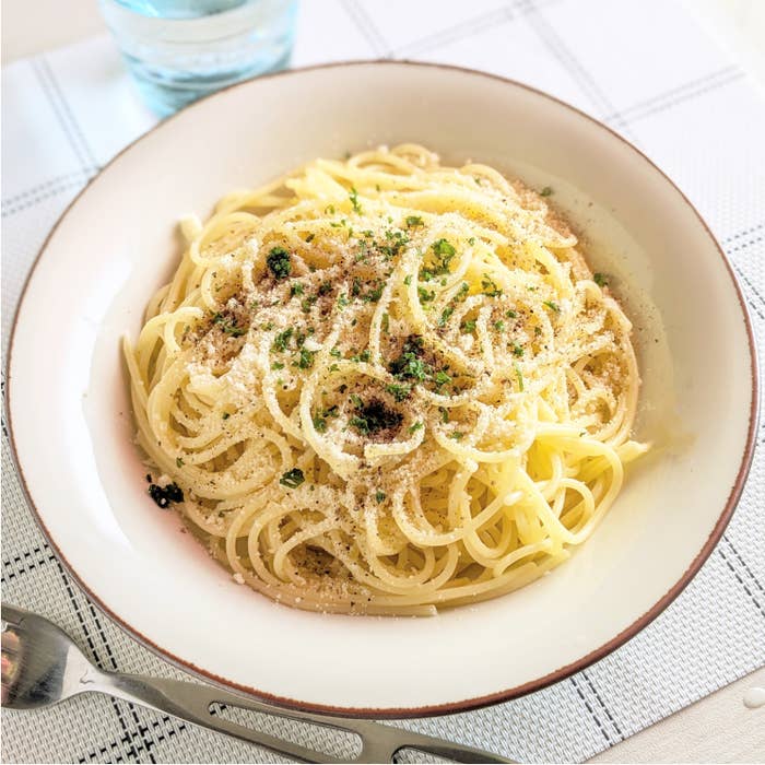 白い皿に盛られたスパゲッティがテーブルに置かれている。隣にはフォーク、グラス。