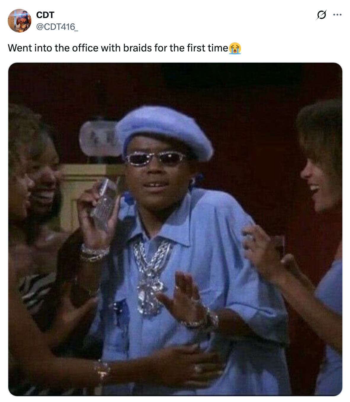 Person in oversized outfit and beret, wearing sunglasses, holding a phone, surrounded by smiling people. Caption implies a humorous scenario