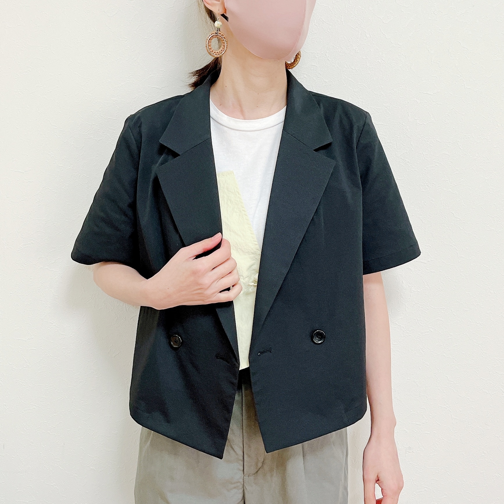 女性がTシャツと短い袖のジャケットを着用し、片手をジャケットの前で持ち上げています。大ぶりのイヤリングを着用。