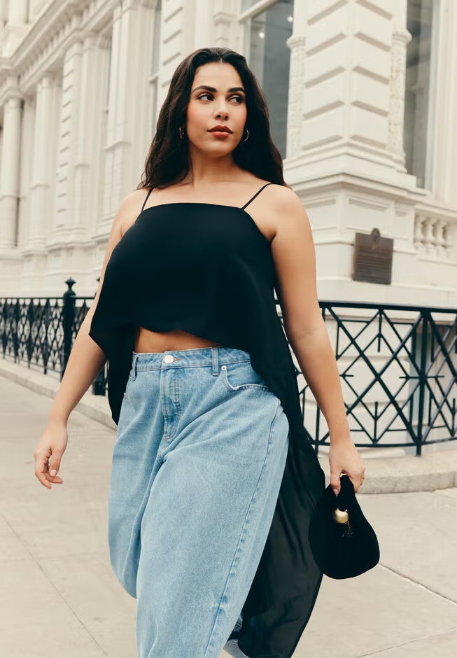 Person in flowy black top and wide-leg jeans walks confidently outside