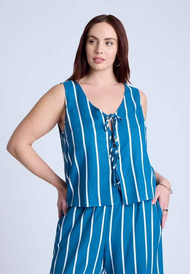 Person wearing a sleeveless, striped top with lace-up detail and matching pants, posing with one hand on hip. Fashion-focused shopping image