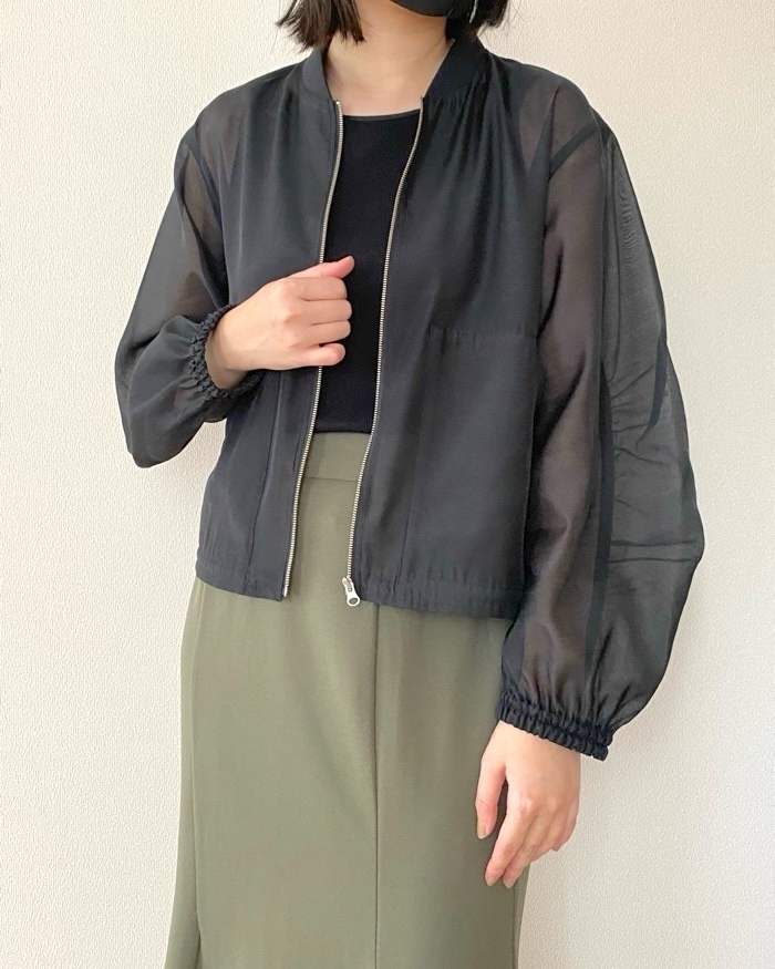 女性がフォーマルな黒いジャケットを着用し、落ち着いた緑のスカートを履いている。